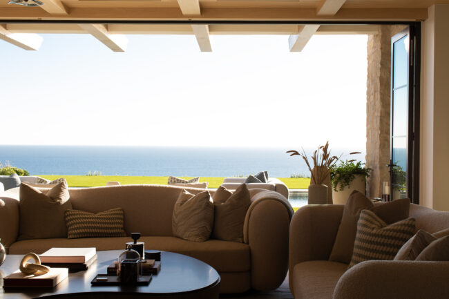 A living room with couches and tables overlooking the ocean.