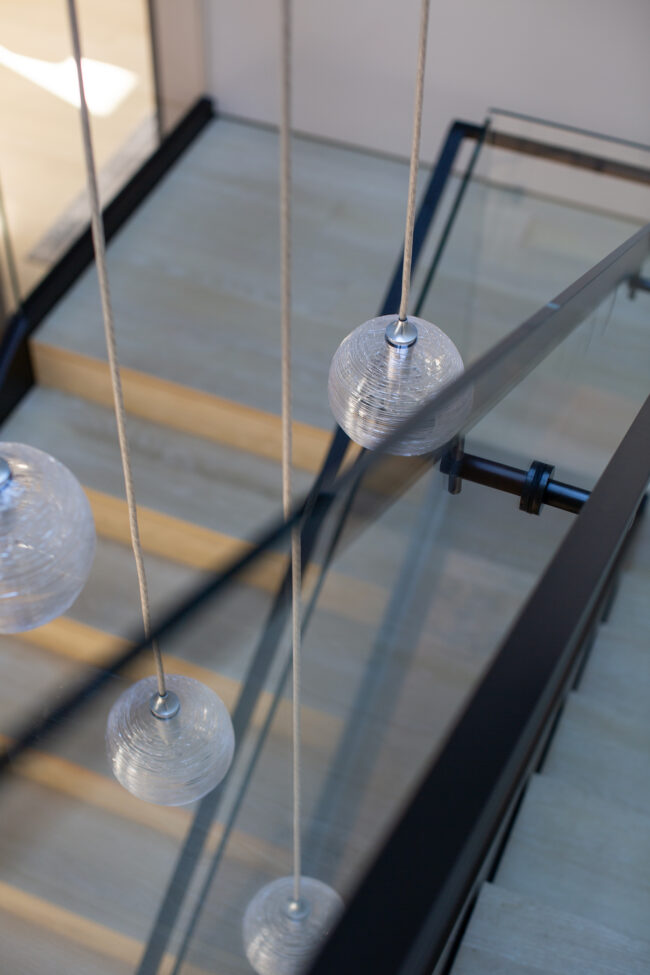 A glass staircase with three lights hanging from the side.