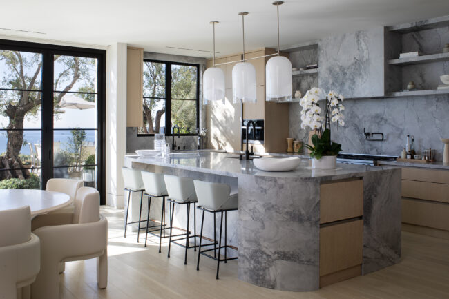 A kitchen with marble counter tops and white chairs.
