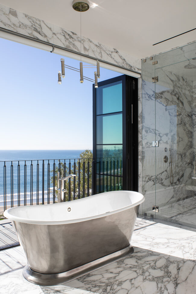 A bathroom with a view of the ocean and a tub.