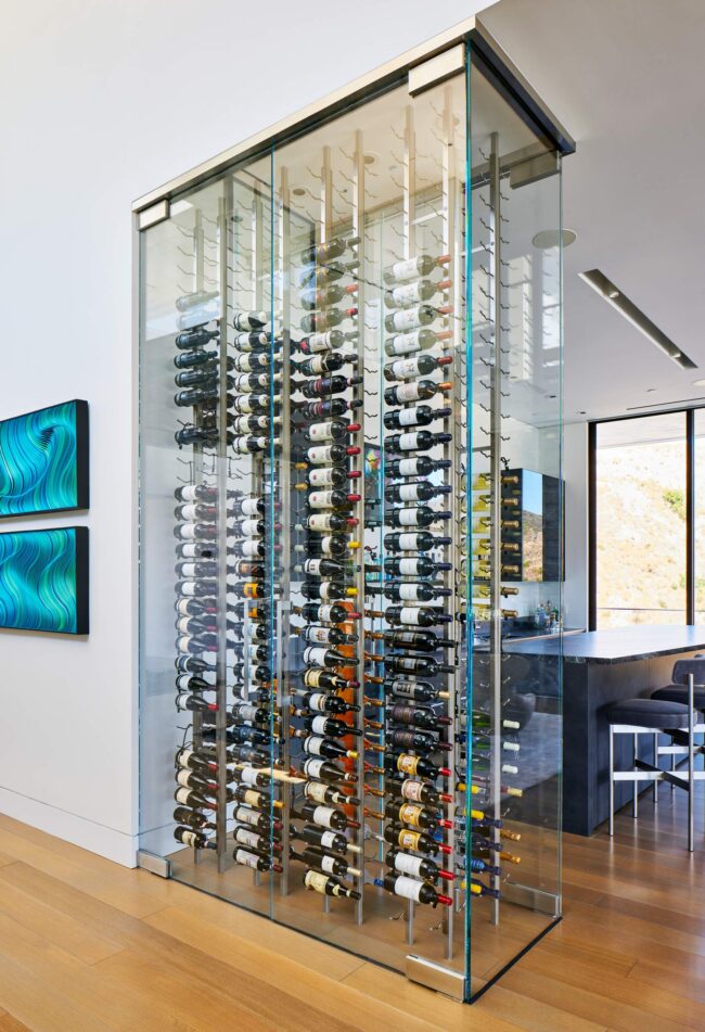 A glass wine rack with many bottles of wine.