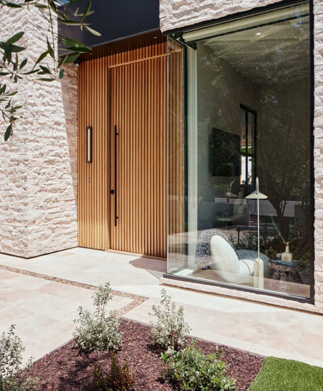 A wooden door with glass windows and plants outside.