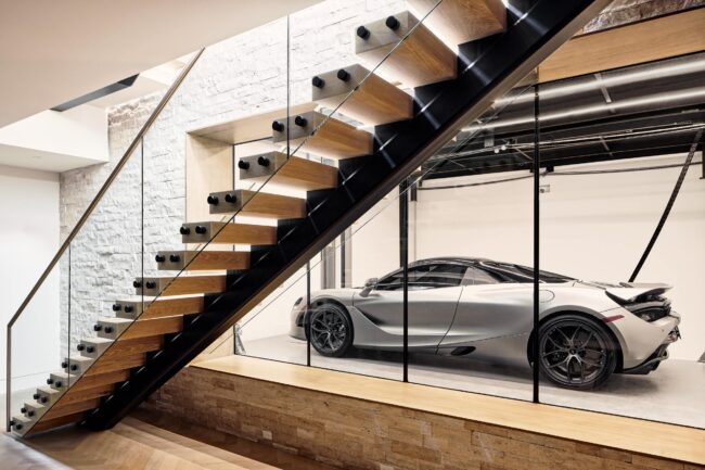 A car is parked in the garage next to stairs.