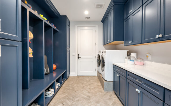 A blue laundry room with white cabinets and a sink.