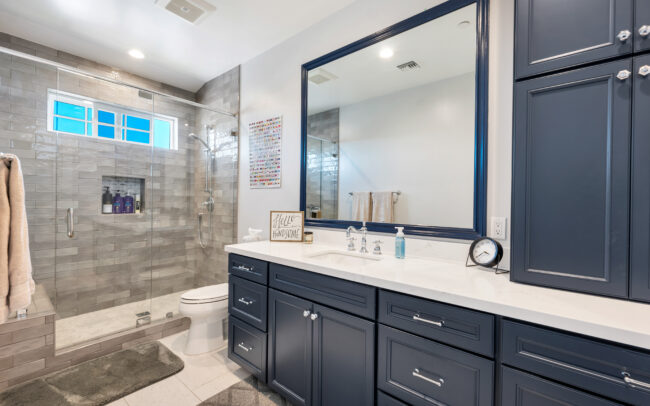 A bathroom with a large mirror and blue cabinets.