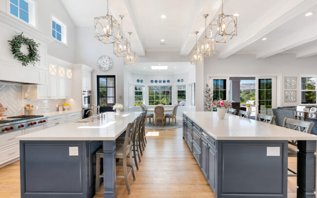 A large kitchen with two large island counters and three chandeliers.